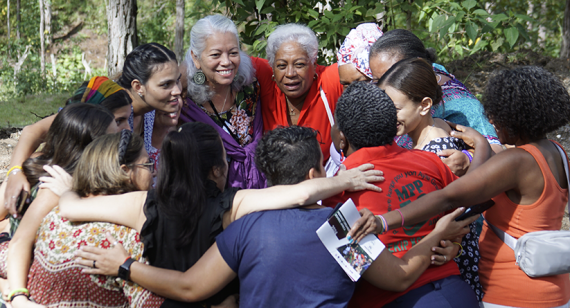 A dozen smiling IFOS participants form a group circle, arms around each other