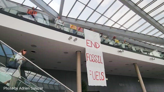 A long banner painted with “END FOSSIL FUELS” is unfurled over a bannister in an atrium in Bonn, Germany