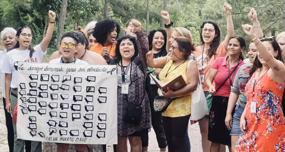 About a dozen people, some with fists raised, stand in a group outside, holding a wall chart.