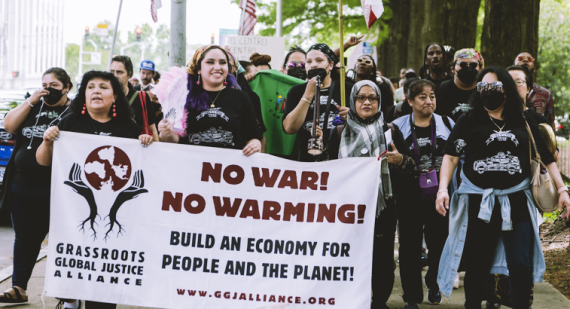 Many people marching outside, holding signs and flags. Text on the front banner: NO WAR! NO WARMING! / Build an economy for people and the planet! / Grassroots Global Justice Alliance / www.ggjalliance.org