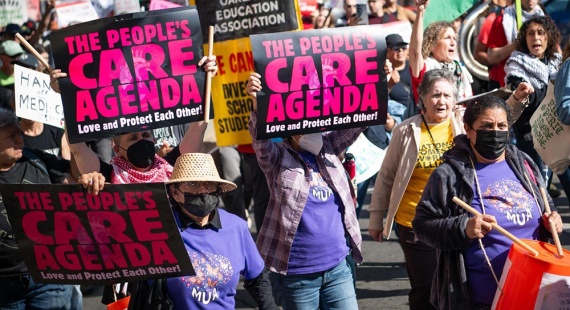 Photo of people marching in a crowd, holding signs with text: The People’s Care Agenda. Love and Protect Each Other!