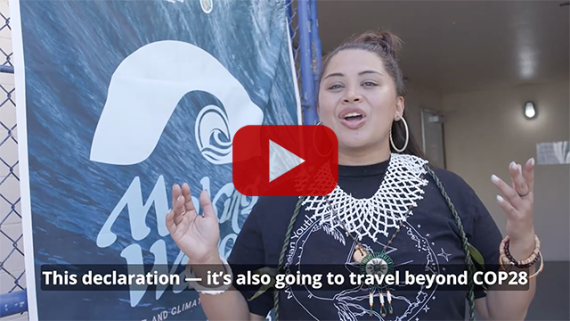 Screenshot of a video, with a person speaking in the foreground and a Making Waves banner in the background. Subtitle says: This declaration — it’s also going to travel beyond COP28